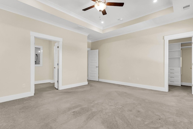 unfurnished bedroom featuring a raised ceiling, ornamental molding, a walk in closet, and light colored carpet