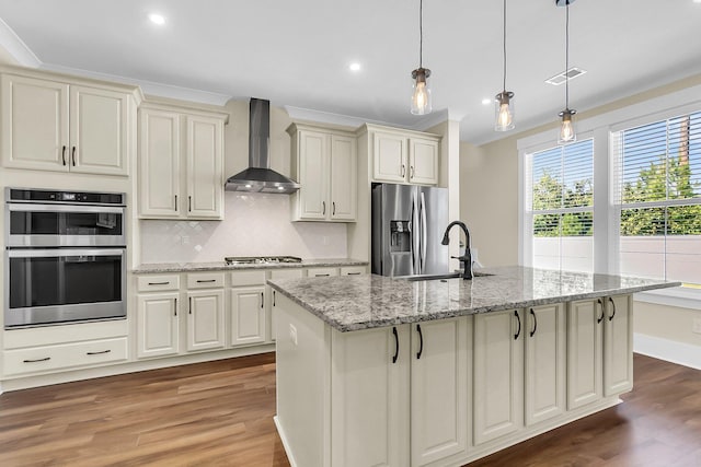 kitchen featuring stainless steel appliances, an island with sink, pendant lighting, and wall chimney exhaust hood