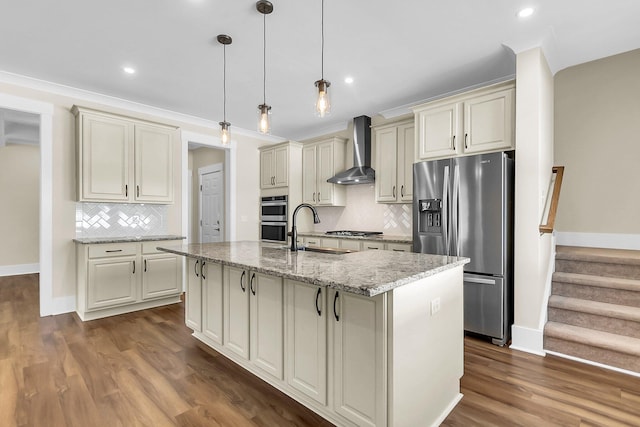 kitchen with an island with sink, appliances with stainless steel finishes, pendant lighting, and wall chimney exhaust hood