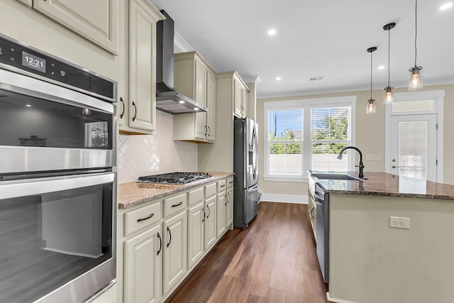 kitchen featuring sink, hanging light fixtures, stainless steel appliances, cream cabinets, and wall chimney exhaust hood