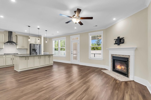 kitchen featuring wall chimney exhaust hood, a center island, hanging light fixtures, stainless steel fridge, and cream cabinetry