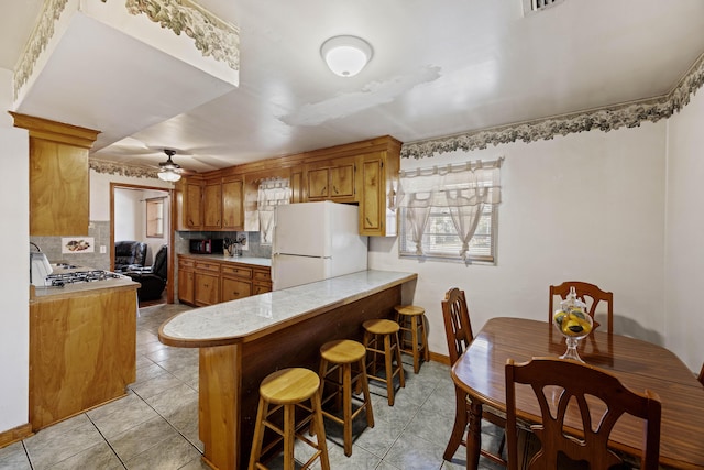 kitchen featuring white refrigerator, ceiling fan, tasteful backsplash, kitchen peninsula, and a breakfast bar area