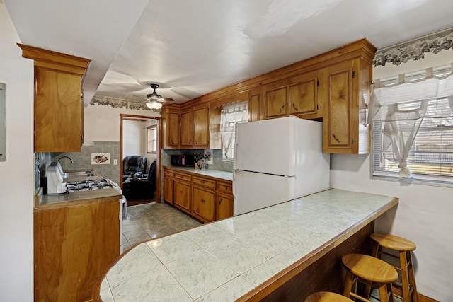 kitchen with a breakfast bar area, white appliances, decorative backsplash, and tile counters