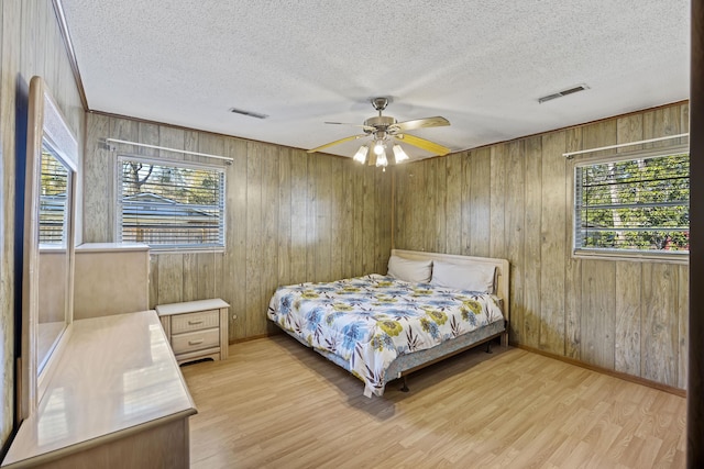 bedroom with ceiling fan, multiple windows, and wood walls