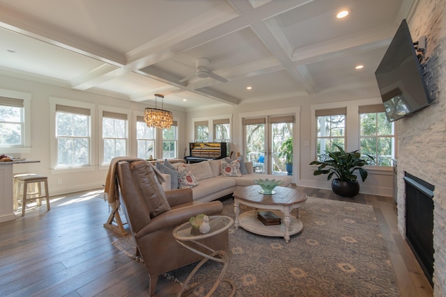 living area featuring beam ceiling, coffered ceiling, a stone fireplace, and wood finished floors