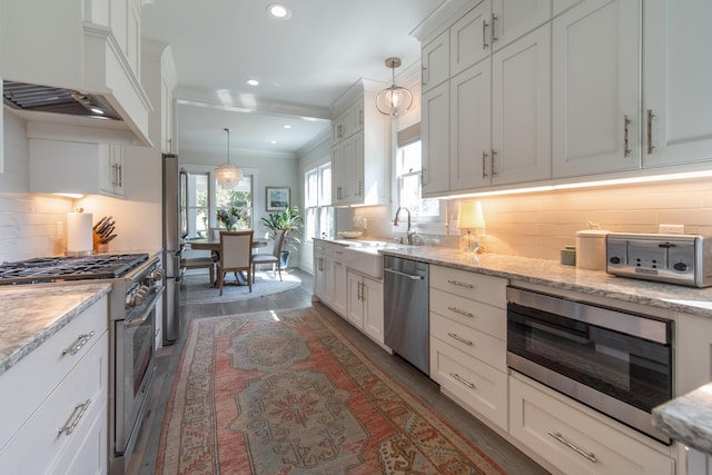 kitchen with light stone counters, pendant lighting, appliances with stainless steel finishes, white cabinetry, and a sink