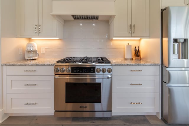 kitchen with stainless steel appliances, custom exhaust hood, white cabinetry, and light stone countertops