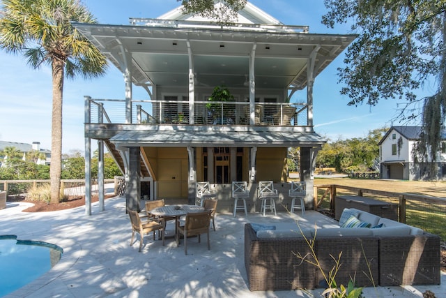 back of property with a balcony, an outdoor pool, an outdoor living space, and a patio