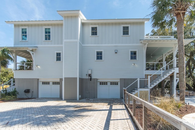 back of property with board and batten siding, decorative driveway, an attached garage, and stairs