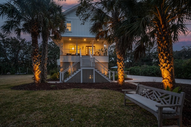 back of property at dusk with covered porch, stairs, and a yard