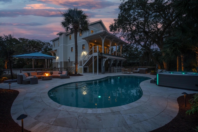 pool at dusk featuring a hot tub, a fenced in pool, an outdoor living space with a fire pit, stairs, and a patio area