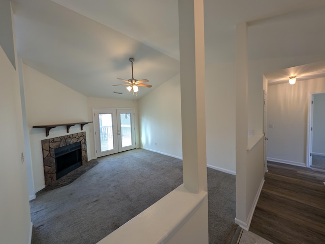 unfurnished living room featuring lofted ceiling, ceiling fan, a fireplace, dark carpet, and french doors