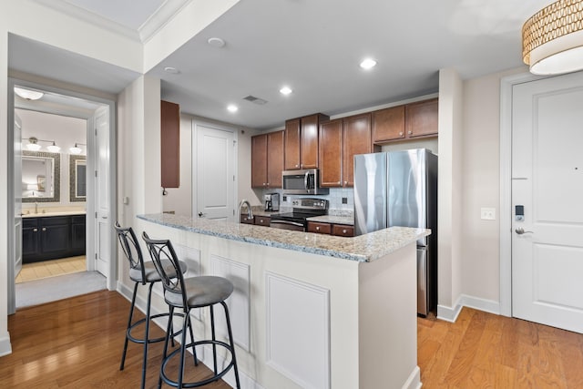 kitchen featuring a kitchen bar, visible vents, appliances with stainless steel finishes, light wood finished floors, and ornamental molding