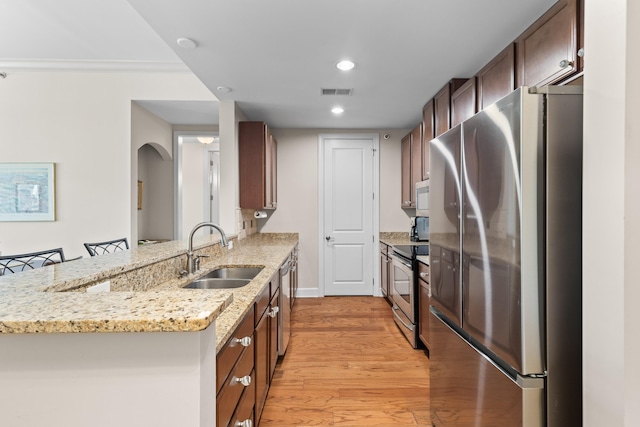 kitchen with a peninsula, arched walkways, a sink, light wood finished floors, and stainless steel appliances