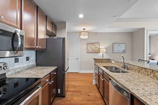 kitchen with light stone countertops, a sink, light wood-style floors, stainless steel appliances, and backsplash