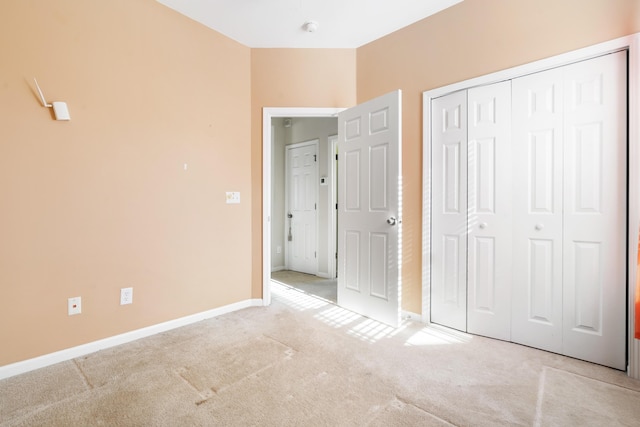 unfurnished bedroom featuring light carpet, a closet, and baseboards