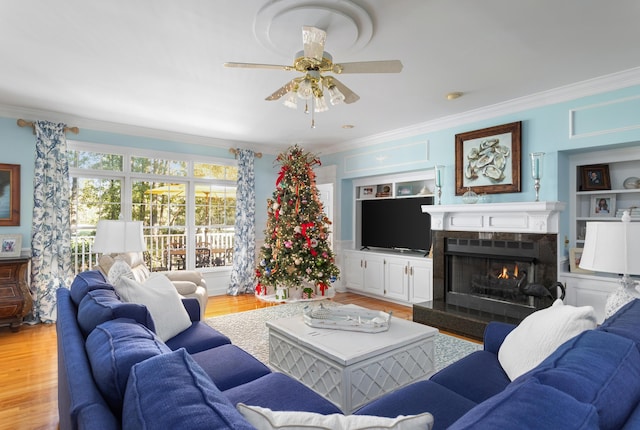 living room featuring built in features, light wood-type flooring, a warm lit fireplace, and crown molding