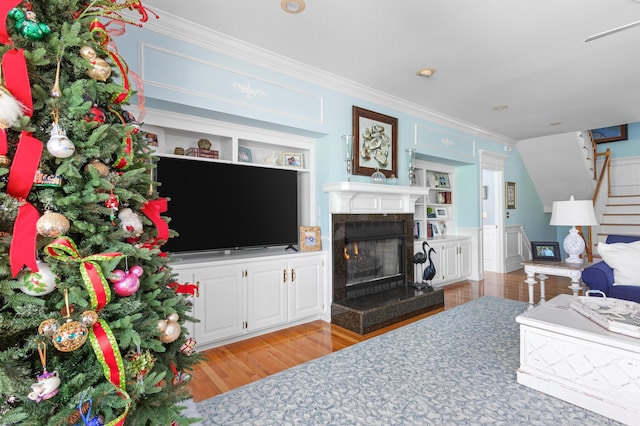 living room featuring stairway, built in shelves, light wood-type flooring, and crown molding