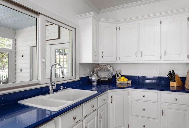 kitchen with dark countertops, white cabinetry, crown molding, and a sink