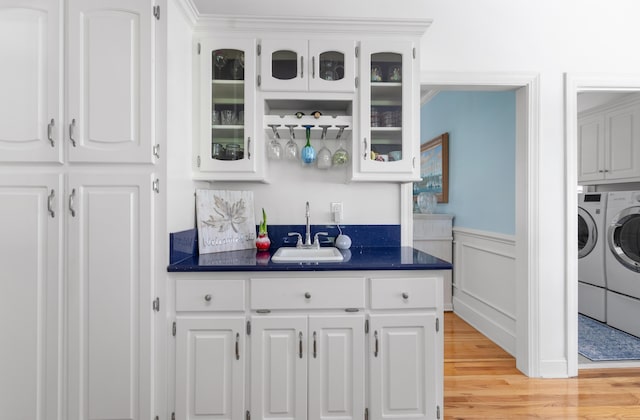 bar with light wood-type flooring, a sink, wainscoting, indoor wet bar, and washing machine and clothes dryer