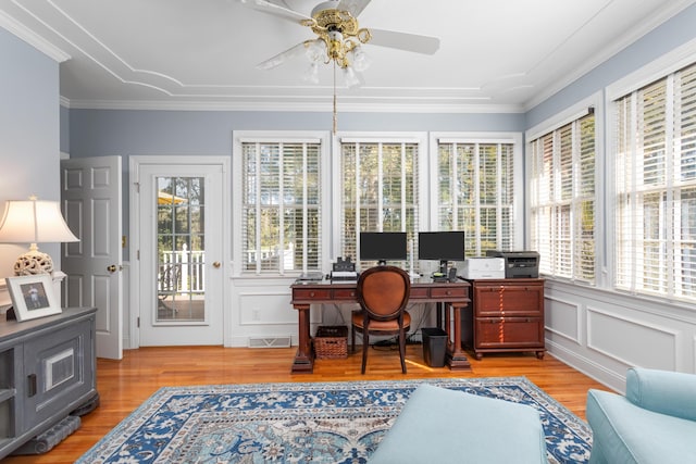 office space with visible vents, light wood finished floors, ceiling fan, crown molding, and a decorative wall