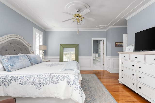 bedroom featuring ceiling fan, a wainscoted wall, ornamental molding, light wood-style flooring, and ensuite bath