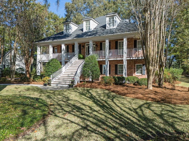 view of front facade with brick siding, stairway, covered porch, and a front lawn