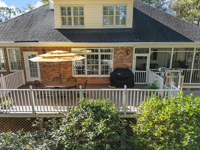 back of house featuring brick siding, a deck, and a sunroom