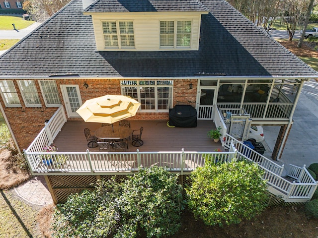 back of house with brick siding, a wooden deck, roof with shingles, and a sunroom