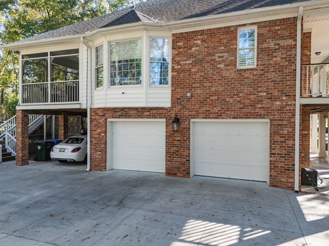 back of property featuring driveway, a garage, brick siding, and a sunroom