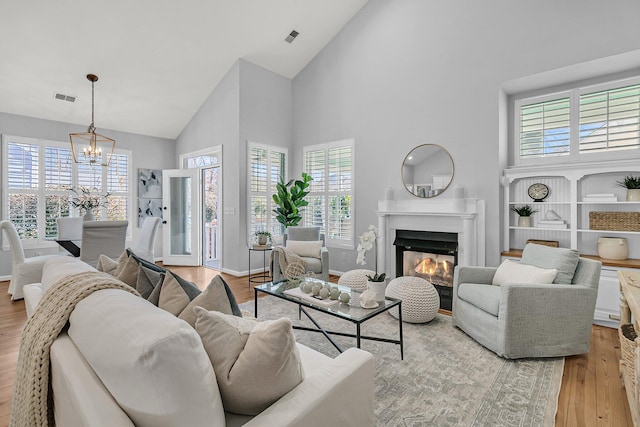 living room featuring light wood-type flooring, visible vents, a fireplace, and an inviting chandelier