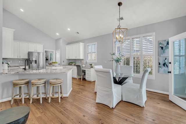 dining room featuring high vaulted ceiling, a notable chandelier, light wood-style flooring, and baseboards