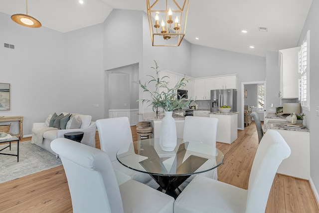 dining space with high vaulted ceiling, light wood-type flooring, visible vents, and an inviting chandelier