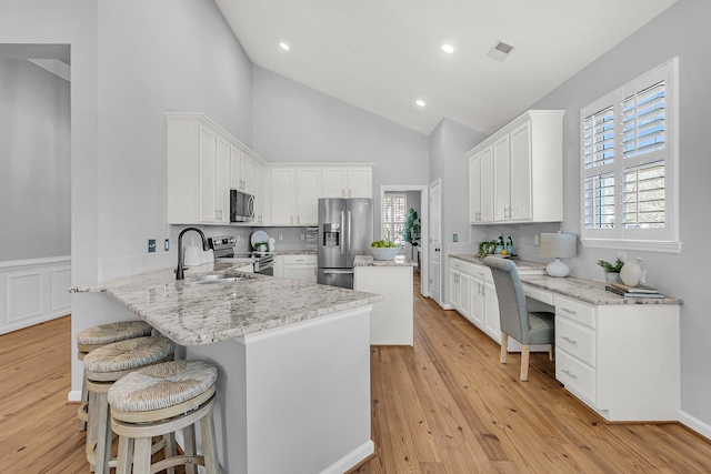 kitchen with light wood-style flooring, a breakfast bar area, a peninsula, stainless steel appliances, and a sink