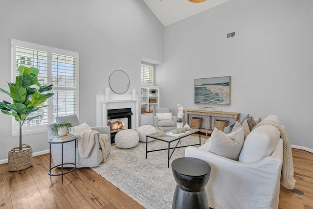 living area featuring a lit fireplace, hardwood / wood-style floors, high vaulted ceiling, and baseboards