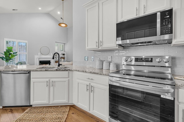 kitchen with appliances with stainless steel finishes, light wood-style floors, white cabinetry, a sink, and a peninsula