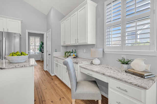 kitchen featuring white cabinets, decorative backsplash, built in study area, lofted ceiling, and freestanding refrigerator