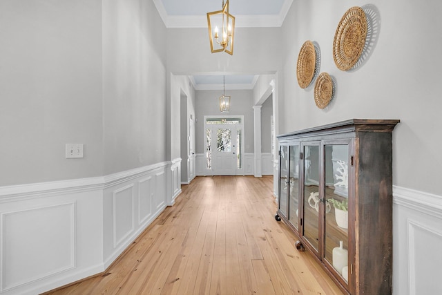 interior space with a decorative wall, ornamental molding, wainscoting, light wood-type flooring, and an inviting chandelier