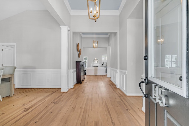 entryway with a decorative wall, a wainscoted wall, ornate columns, light wood finished floors, and crown molding