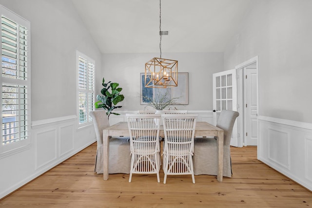 dining area featuring light wood-type flooring, a wainscoted wall, lofted ceiling, and an inviting chandelier