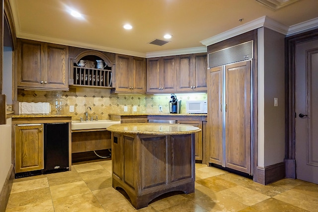 kitchen with paneled built in fridge, crown molding, sink, decorative backsplash, and a kitchen island