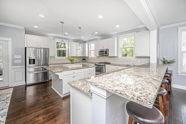 kitchen featuring stainless steel appliances, a breakfast bar area, a peninsula, dark wood finished floors, and ornamental molding