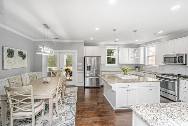 kitchen featuring stainless steel appliances, crown molding, a kitchen island, white cabinetry, and backsplash
