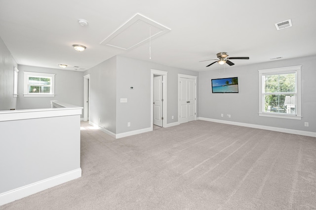 spare room with attic access, light colored carpet, baseboards, and ceiling fan