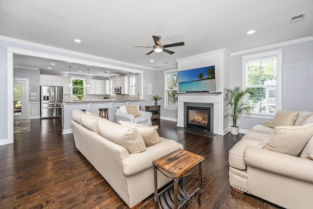 living area with ornamental molding, ceiling fan, baseboards, dark wood-style flooring, and a fireplace with flush hearth