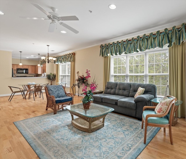 living room with light hardwood / wood-style floors, a healthy amount of sunlight, crown molding, and ceiling fan with notable chandelier