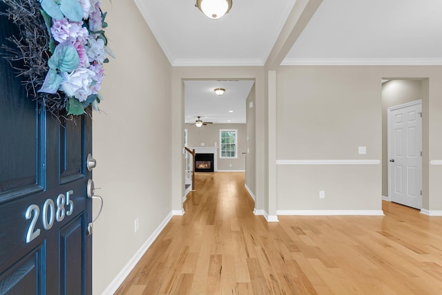 entrance foyer with a glass covered fireplace, crown molding, baseboards, and wood finished floors