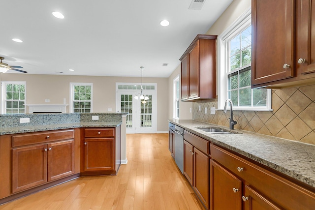 kitchen with light stone counters, a sink, brown cabinets, dishwasher, and decorative light fixtures