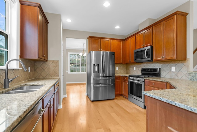 kitchen featuring brown cabinets, light wood finished floors, stainless steel appliances, a sink, and light stone countertops