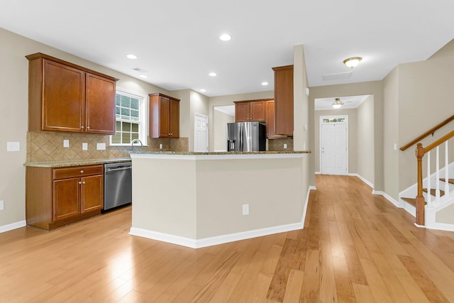 kitchen with a sink, light wood-style floors, appliances with stainless steel finishes, brown cabinets, and light stone countertops